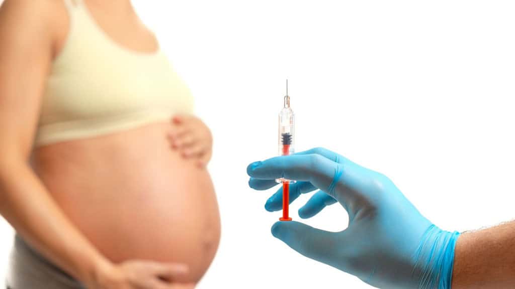 Mão de médico se preparando para injetar anticoagulantes na barriga de uma mulher grávida, isolada em fundo branco