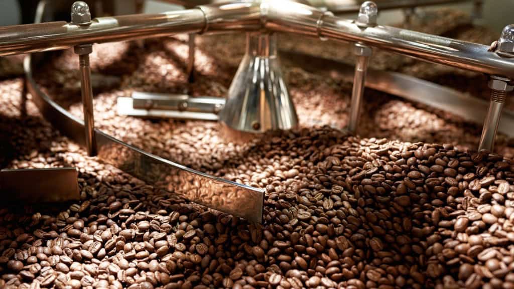 Grãos de café torrados naturalmente misturando-se no misturador da máquina de torrefação industrial na fábrica.