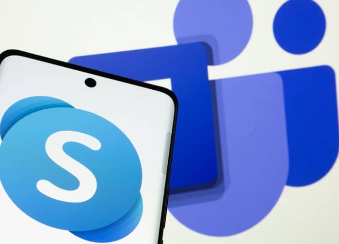 Celular com logotipo do Skype na tela na frente de monitor exibindo logotipo do Microsoft Teams