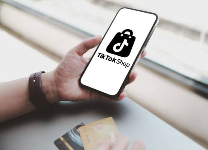 Pessoa segura com uma mão celular com logomarca da TikTok na tela enquanto segura cartões de crédito com a outra mão