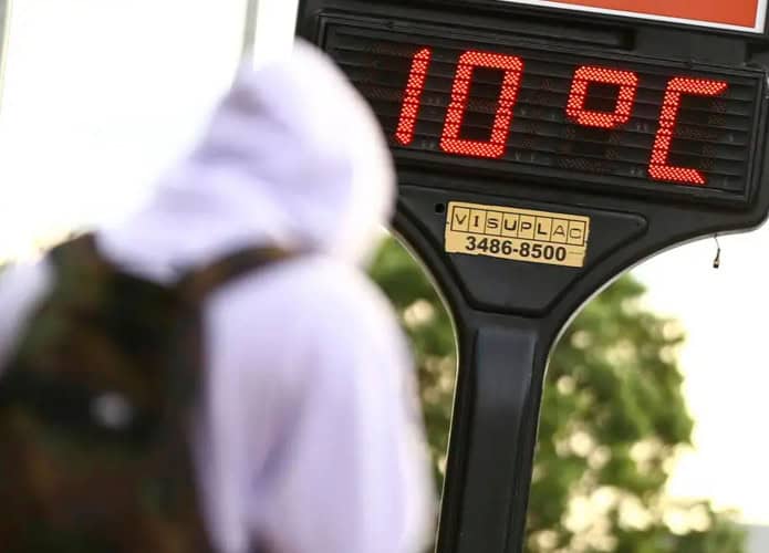 Pessoa de moletom passando por termômetro que marca 10 graus Celsius em dia frio