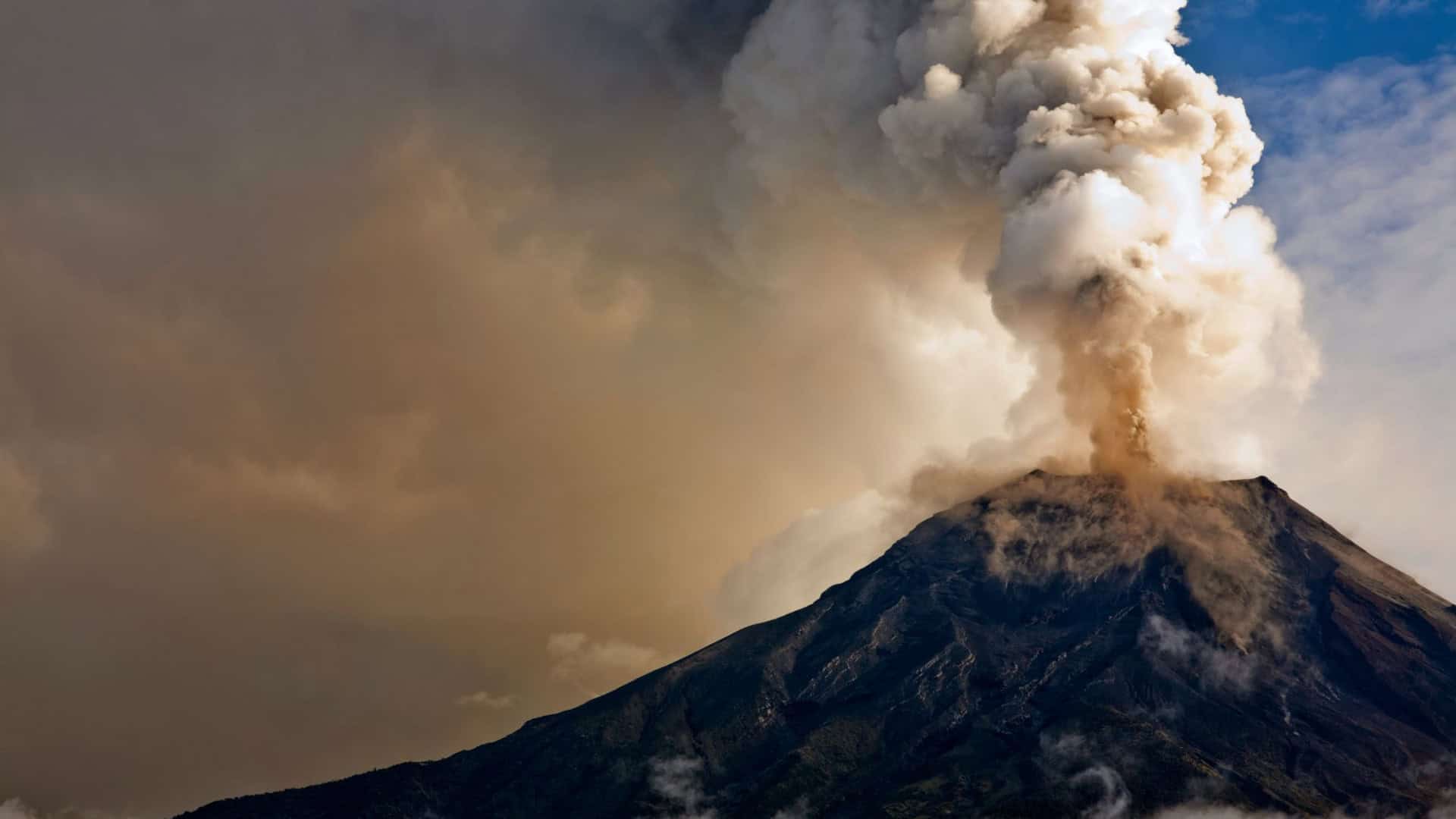 Vulcão em erupção com nuvens ao fundo