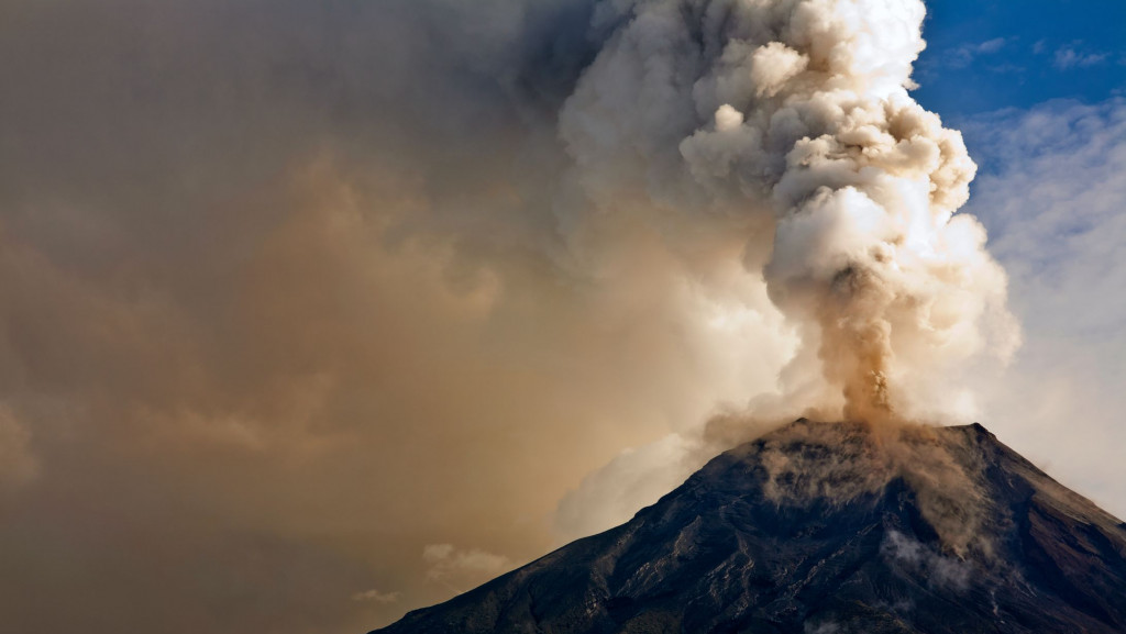 Vulcão em erupção com nuvens ao fundo