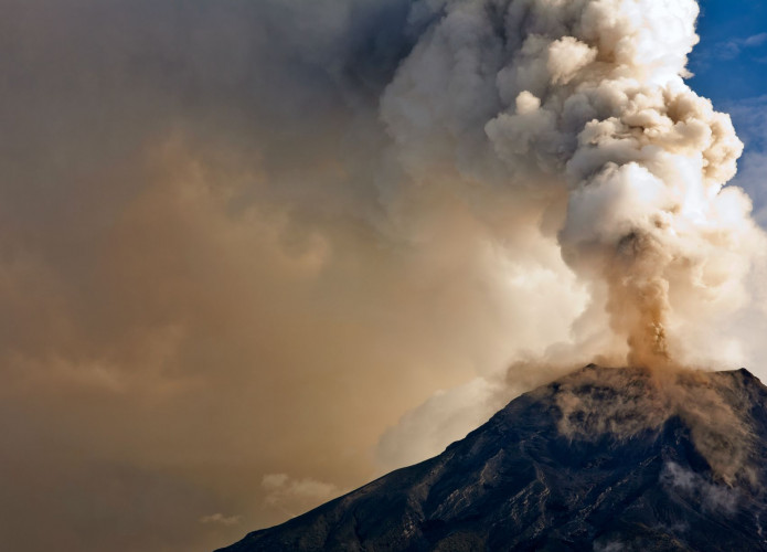 Vulcão em erupção com nuvens ao fundo