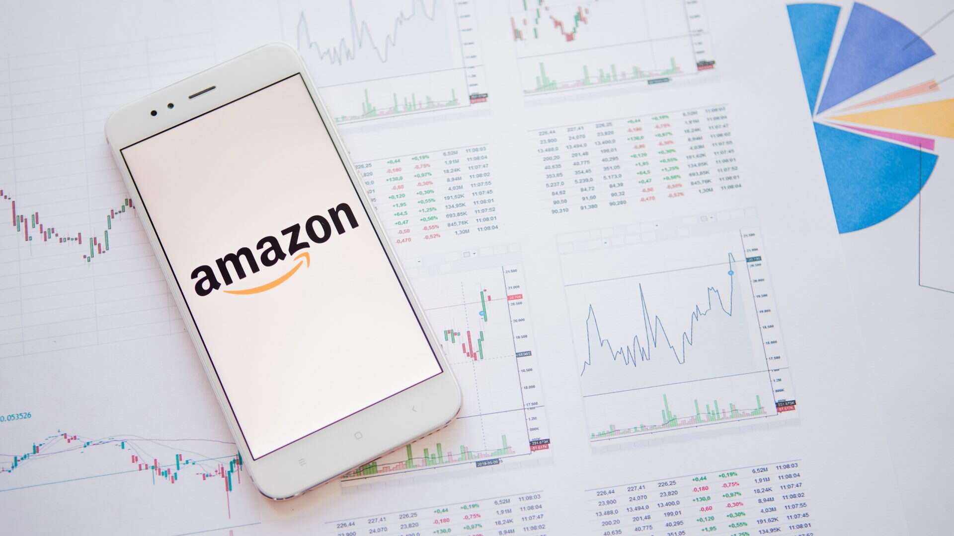 Logo da Amazon em uma tela de smartphone em cima de várias folhas de papel com gráficos e números