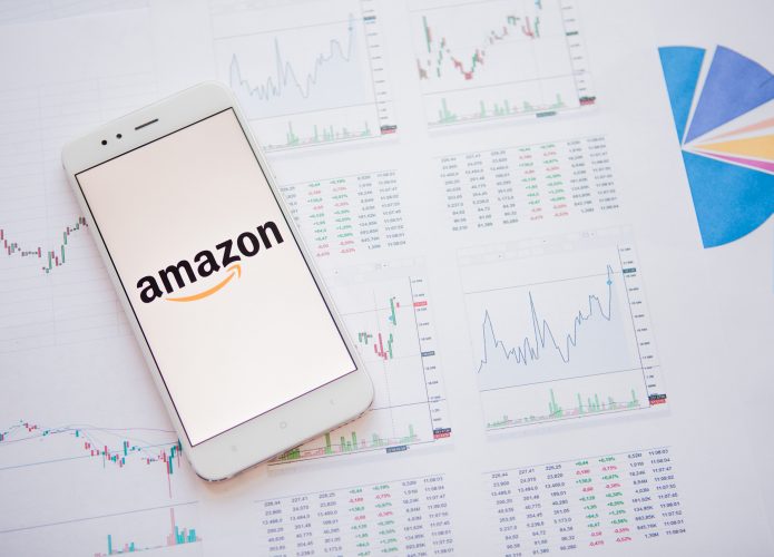 Logo da Amazon em uma tela de smartphone em cima de várias folhas de papel com gráficos e números