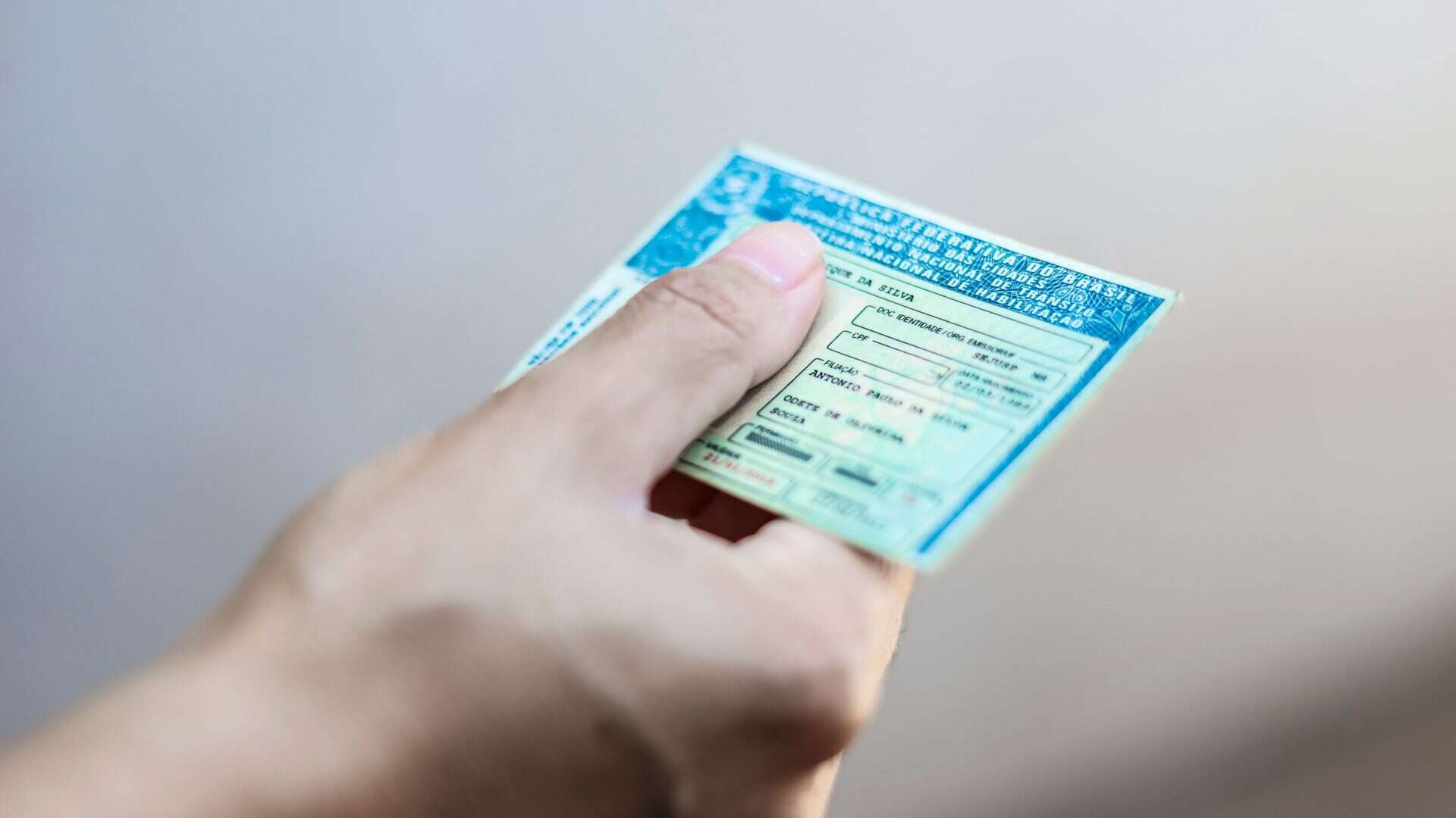 Imagem ilustrativa de mão segurando a CNH (Carteira Nacional de Habilitação)