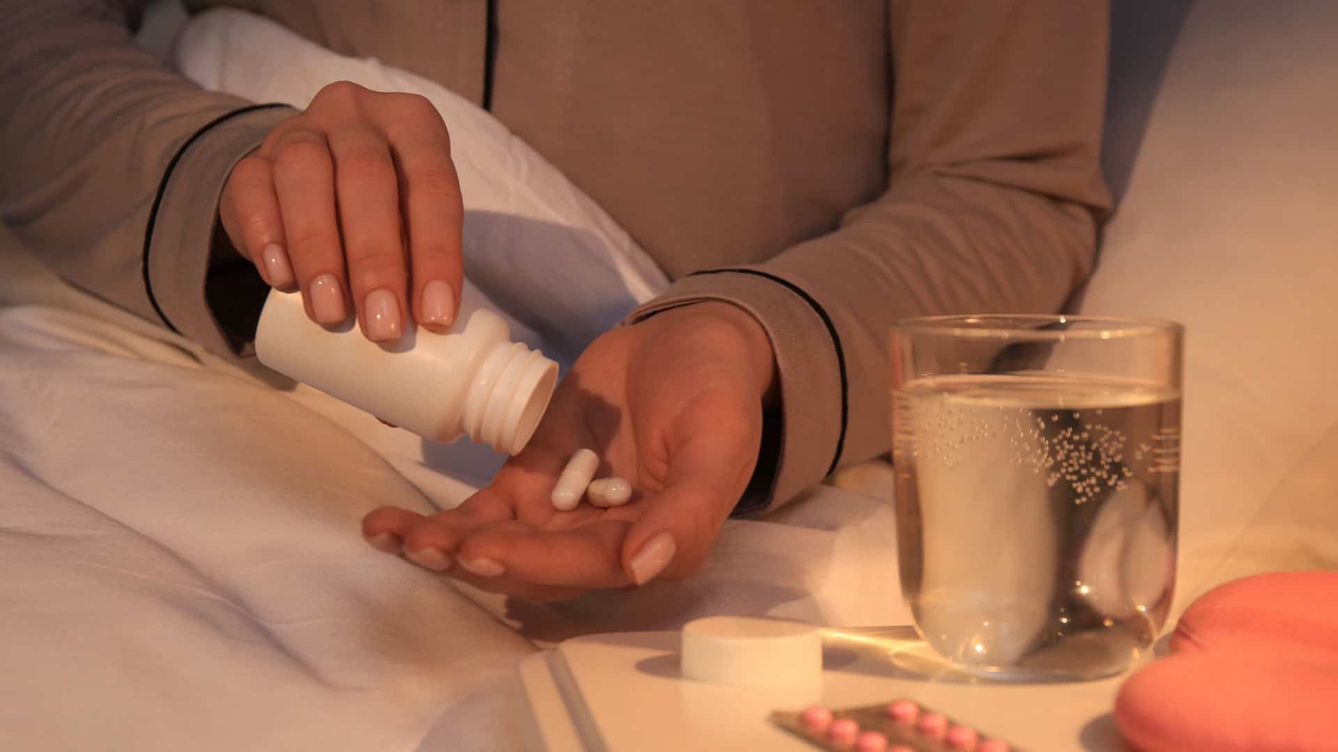 Mulher tomando comprimidos à noite deitada na cama