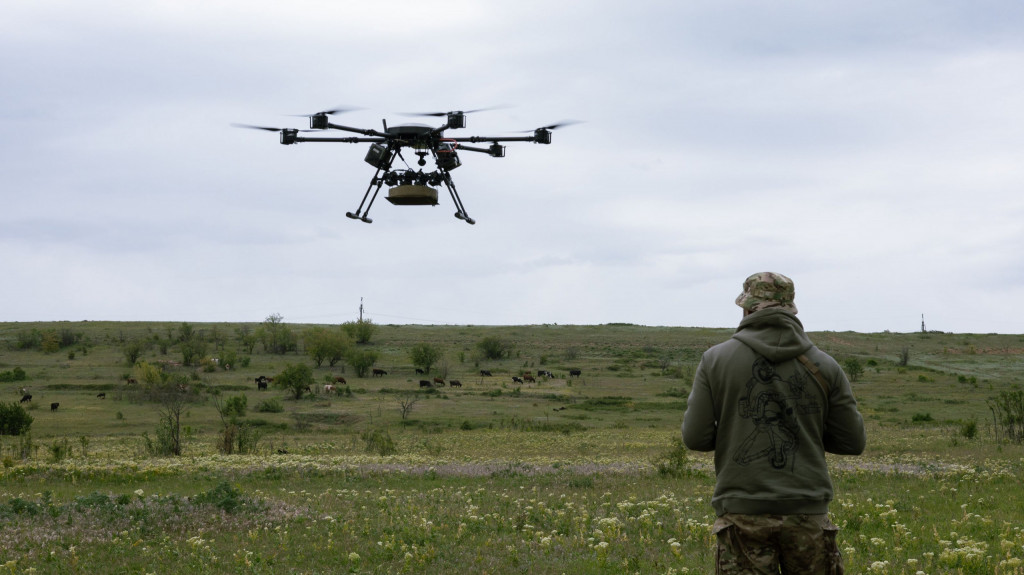 Drone militar voa no céu e um soldado está por perto e o controla