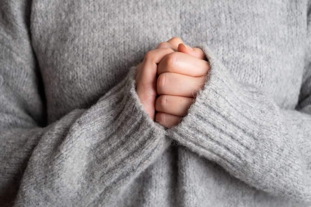 Mulher de blusa de frio com as mãos unidas uma na outra