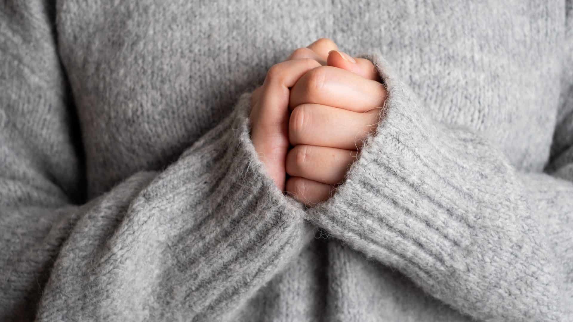 Mulher de blusa de frio com as mãos unidas uma na outra