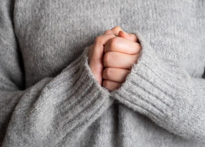 Mulher de blusa de frio com as mãos unidas uma na outra