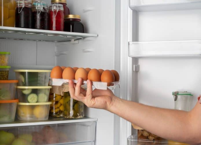 pessoa pegando ovos de uma geladeira com diversos alimentos