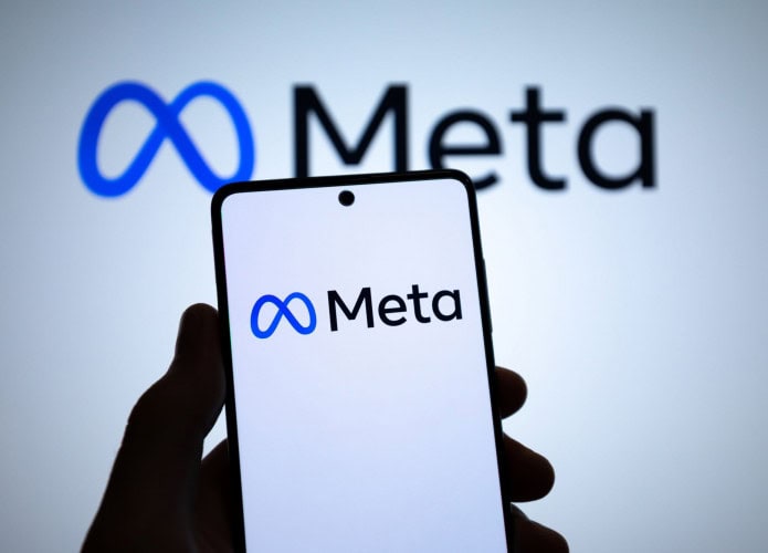 Logo da Meta em um smartphone e ao fundo, em uma tela grande