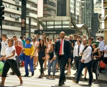 Várias pessoas atravessando a rua em frente a uma estação de metrô