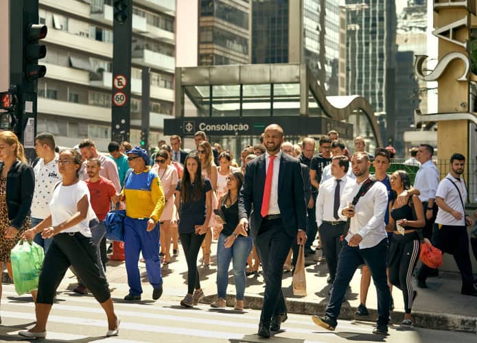 Várias pessoas atravessando a rua em frente a uma estação de metrô
