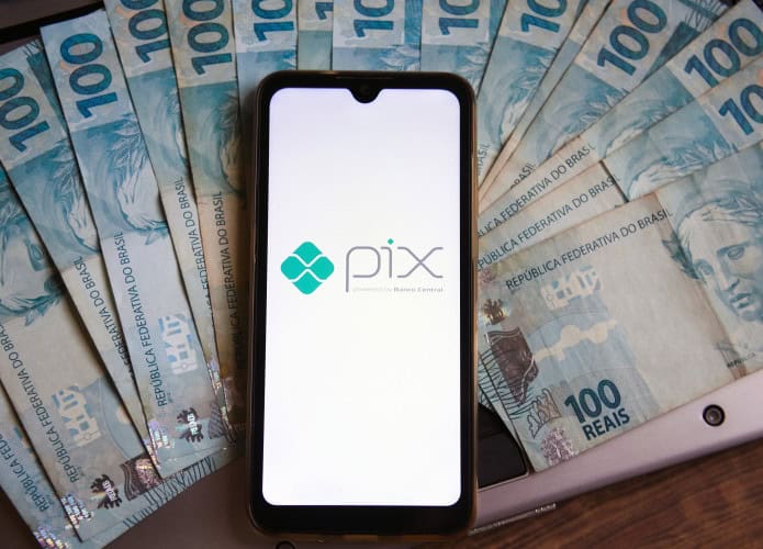 Logo do Pix na tela de um smartphone; debaixo dele, várias notas de R$ 100