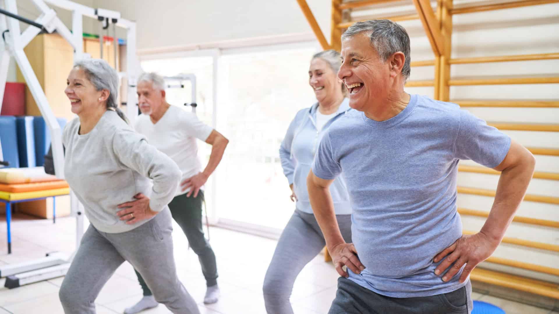 Homens e mulheres idosos felizes se exercitando com as mãos nos quadris durante a aula de exercícios no centro de reabilitação