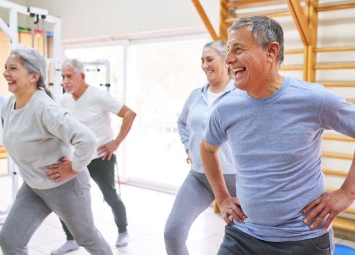 Homens e mulheres idosos felizes se exercitando com as mãos nos quadris durante a aula de exercícios no centro de reabilitação