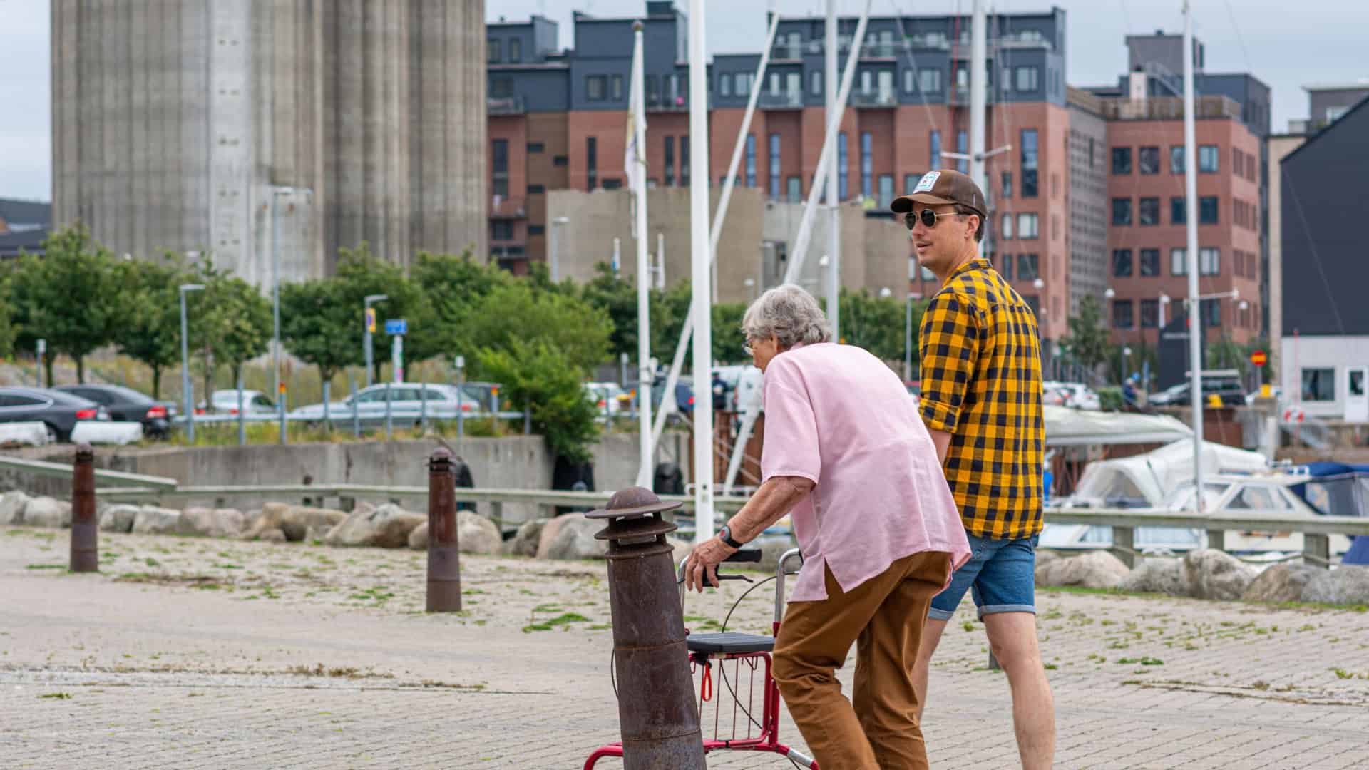 Malmö, Suécia - 14 de julho de 2020: Foto de homem jovem andando com idosa com costas curvadas e andador.