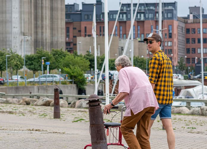Malmö, Suécia - 14 de julho de 2020: Foto de homem jovem andando com idosa com costas curvadas e andador.