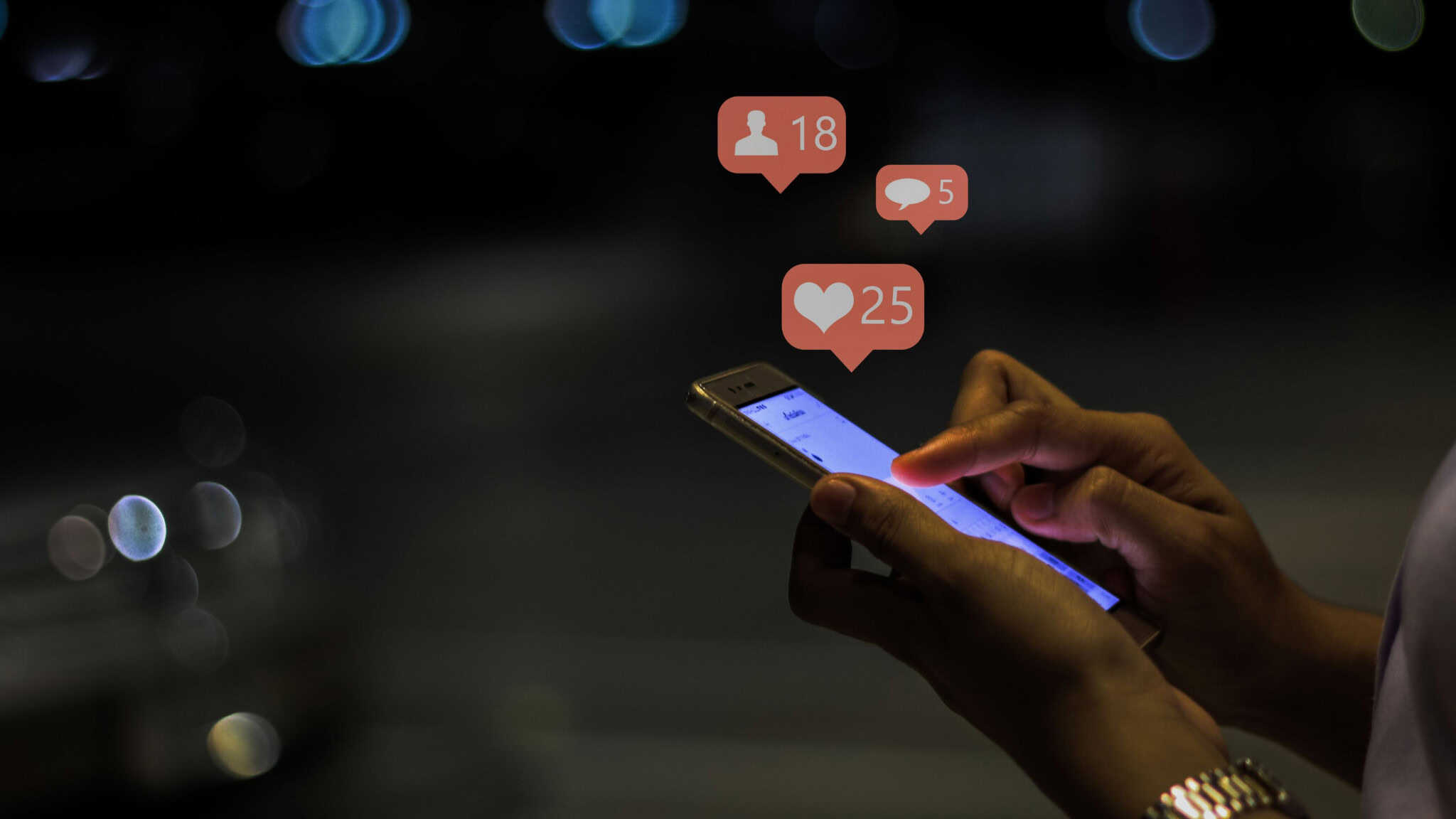 Pessoa mexendo em celular enquanto balões de curtidas, comentários e novos seguidores de redes sociais brotam da tela