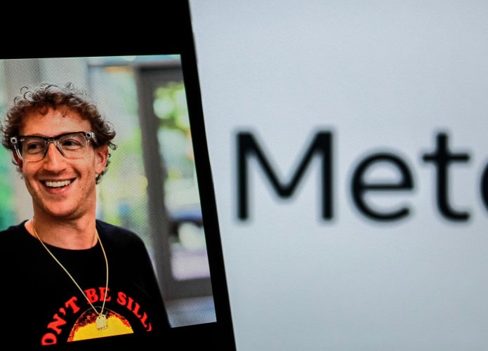 Celular exibindo foto de Mark Zuckerberg colocado em frente tela exibindo logomarca da Meta