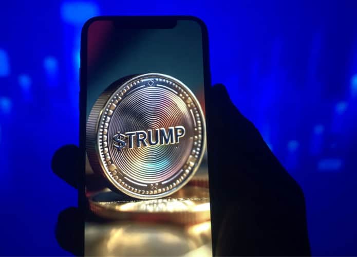 Pessoa segurando celular exibindo imagem de moeda com nome de Trump