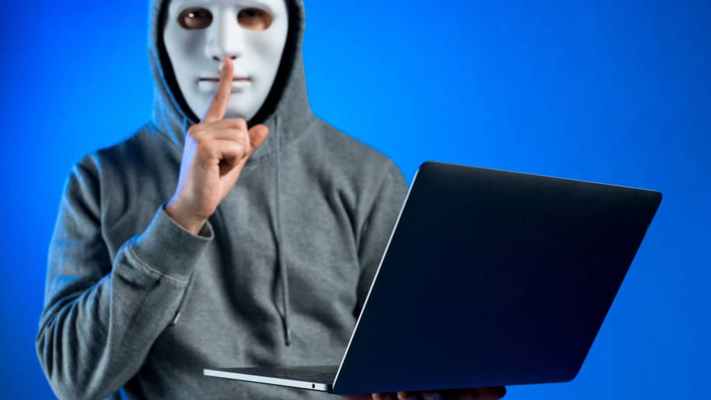 Homem mascarado segura notebook e faz gesto de silêncio