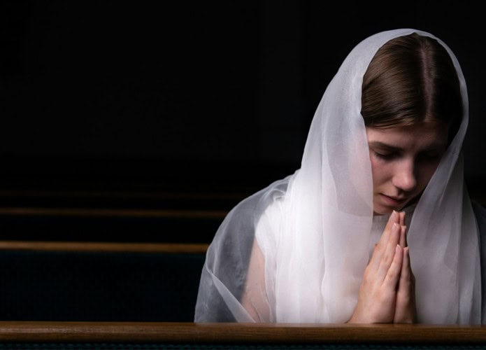 mulher jovem com o véu na cabeça em uma igreja, fazendo oração