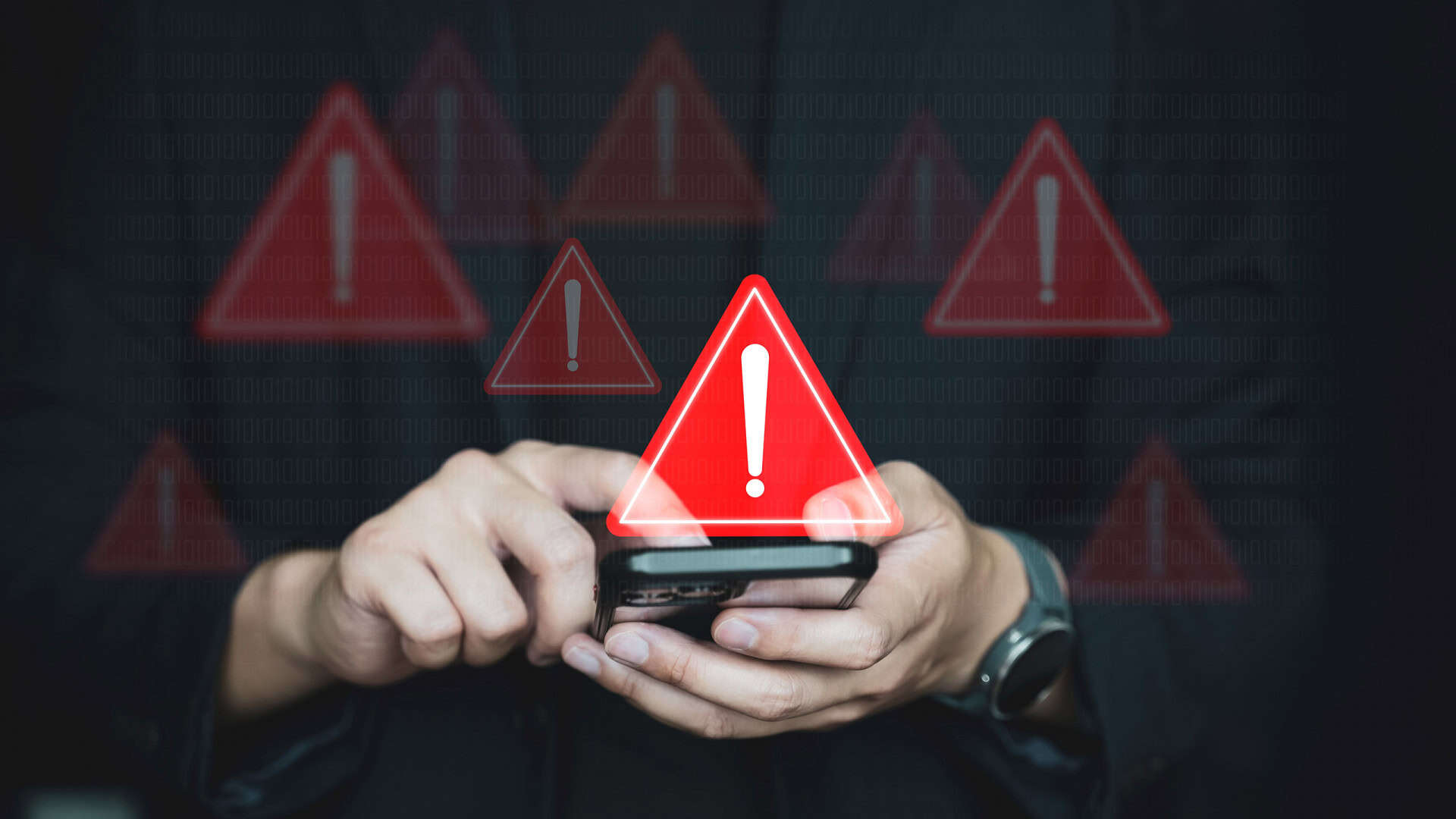 Vários sinais de alerta pairando em cima de um smartphone que está na mão de uma pessoa