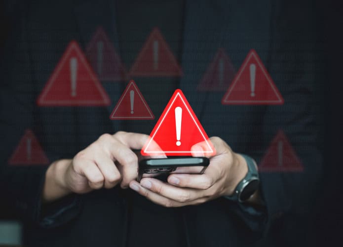 Vários sinais de alerta pairando em cima de um smartphone que está na mão de uma pessoa