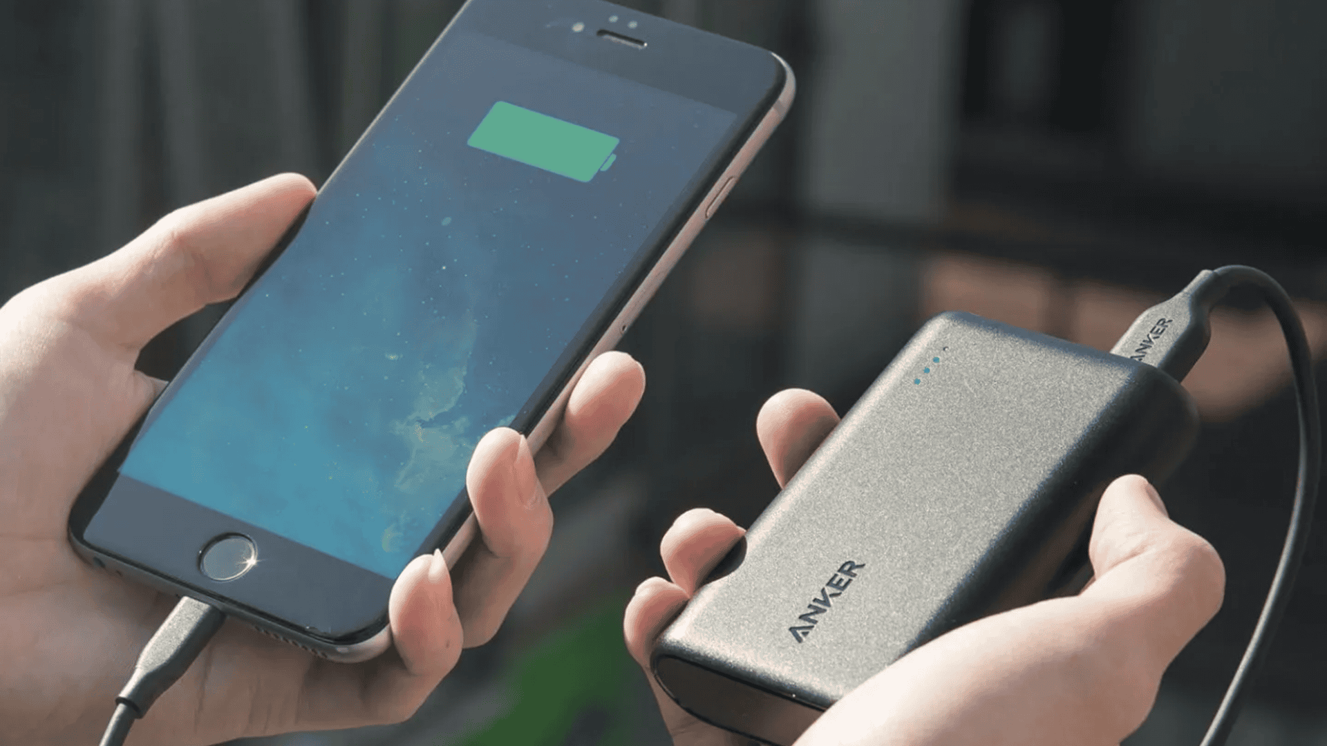 Pessoa segurando um celular e uma bateria portártil da Anker