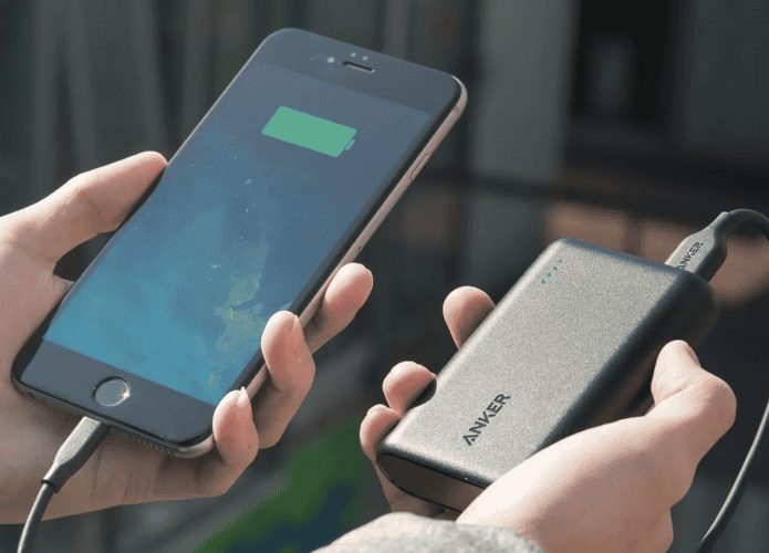 Pessoa segurando um celular e uma bateria portártil da Anker