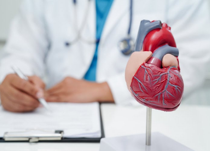 Médico cardiologista com modelo de coração em mesa de clínica