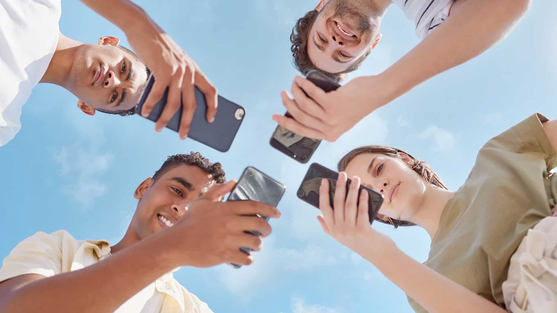 Quatro garotos sendo vistos de baixo com celulares em suas mãos
