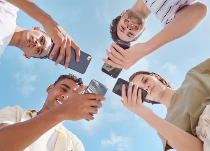 Quatro garotos sendo vistos de baixo com celulares em suas mãos