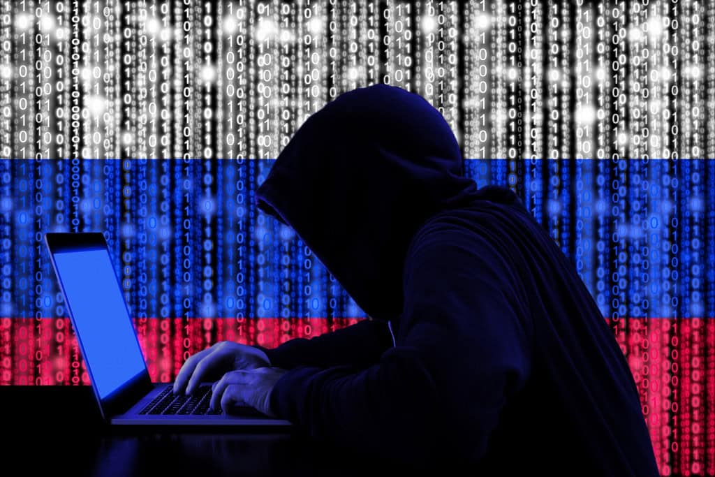 Hacker nas sombras, de perfil e com a bandeira russa atrás