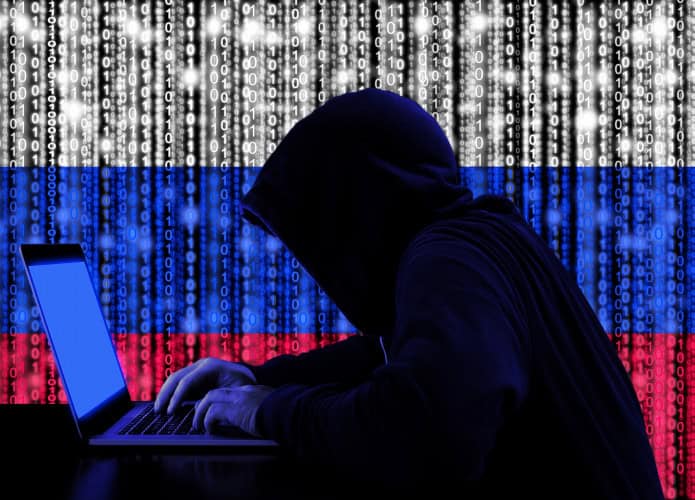 Hacker nas sombras, de perfil e com a bandeira russa atrás