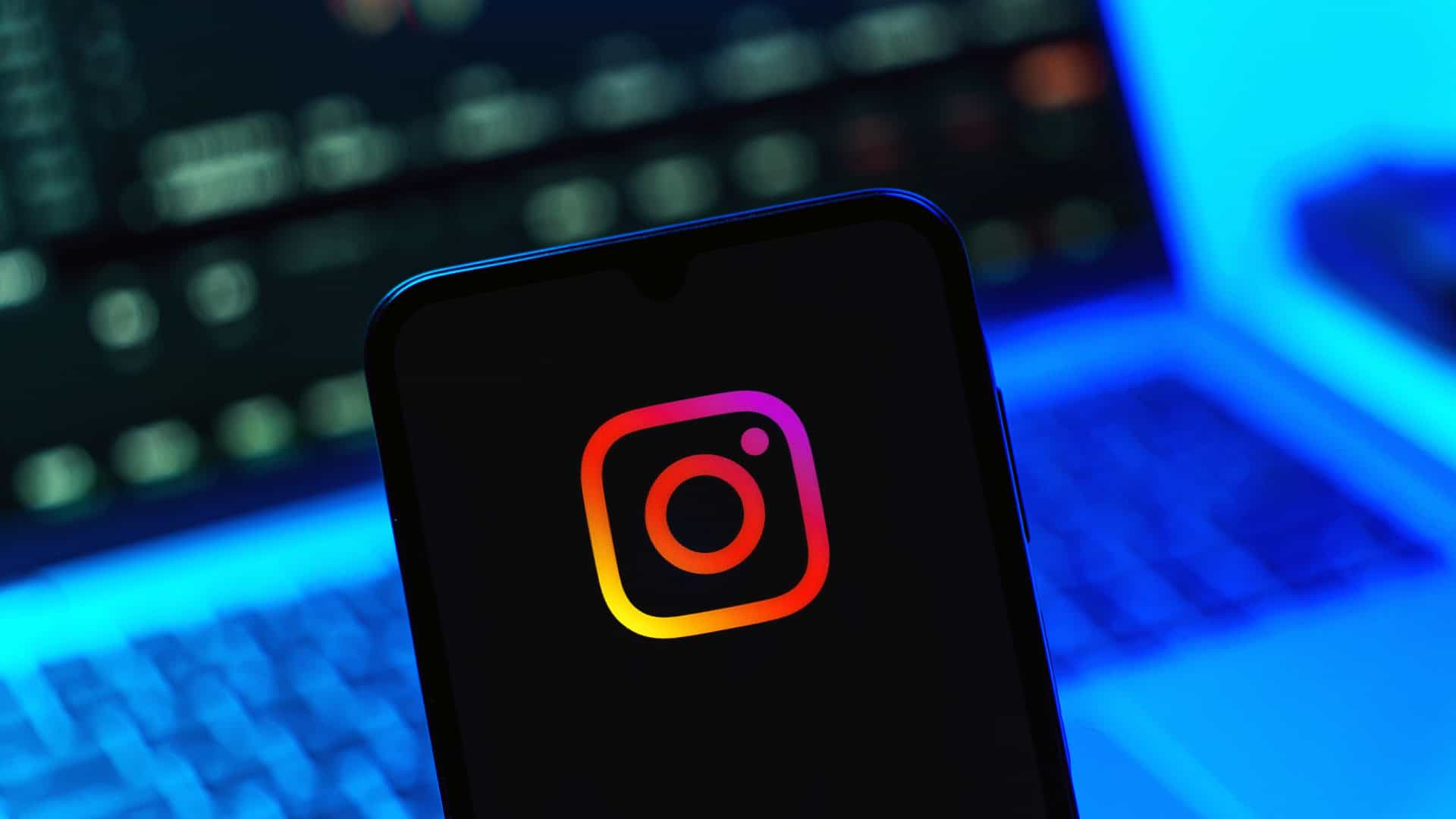 Logo do Instagram em um smartphone com um notebook desfocado ao fundo