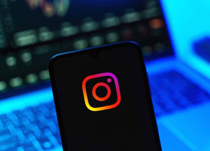 Logo do Instagram em um smartphone com um notebook desfocado ao fundo