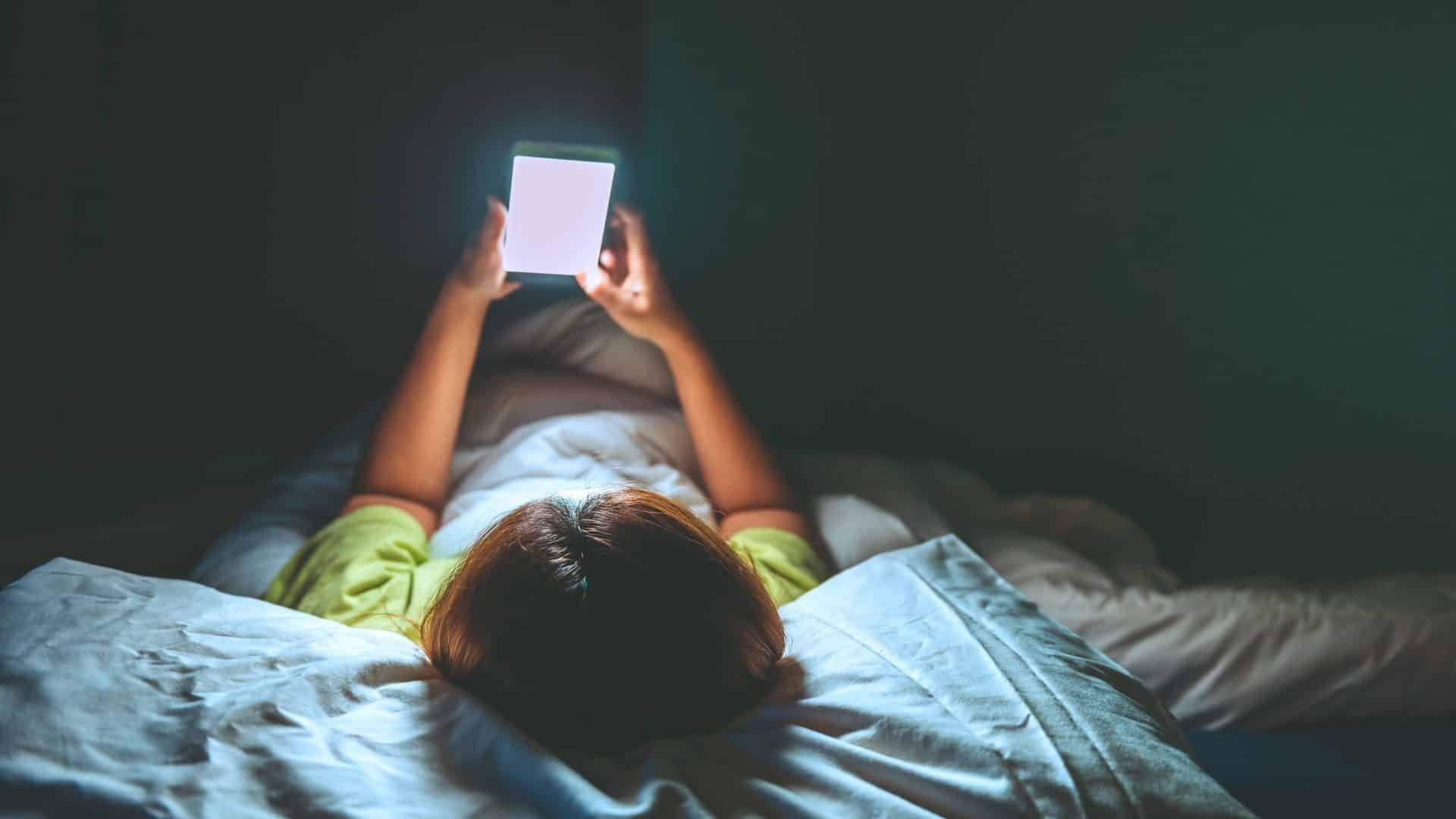 Mulher asiática jogando no smartphone na cama à noite.
