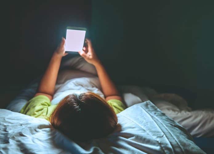 Mulher asiática jogando no smartphone na cama à noite.