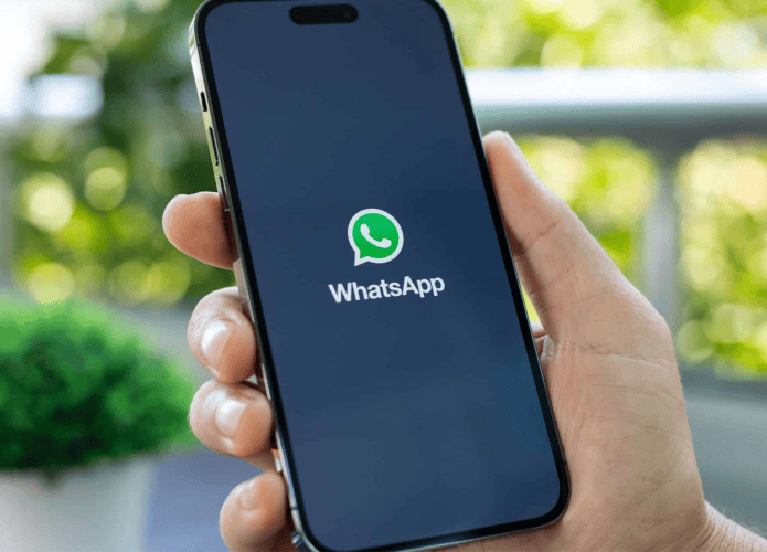 Pessoa segurando iPhone que está abrindo WhatsApp e exibe logomarca do aplicativo na tela
