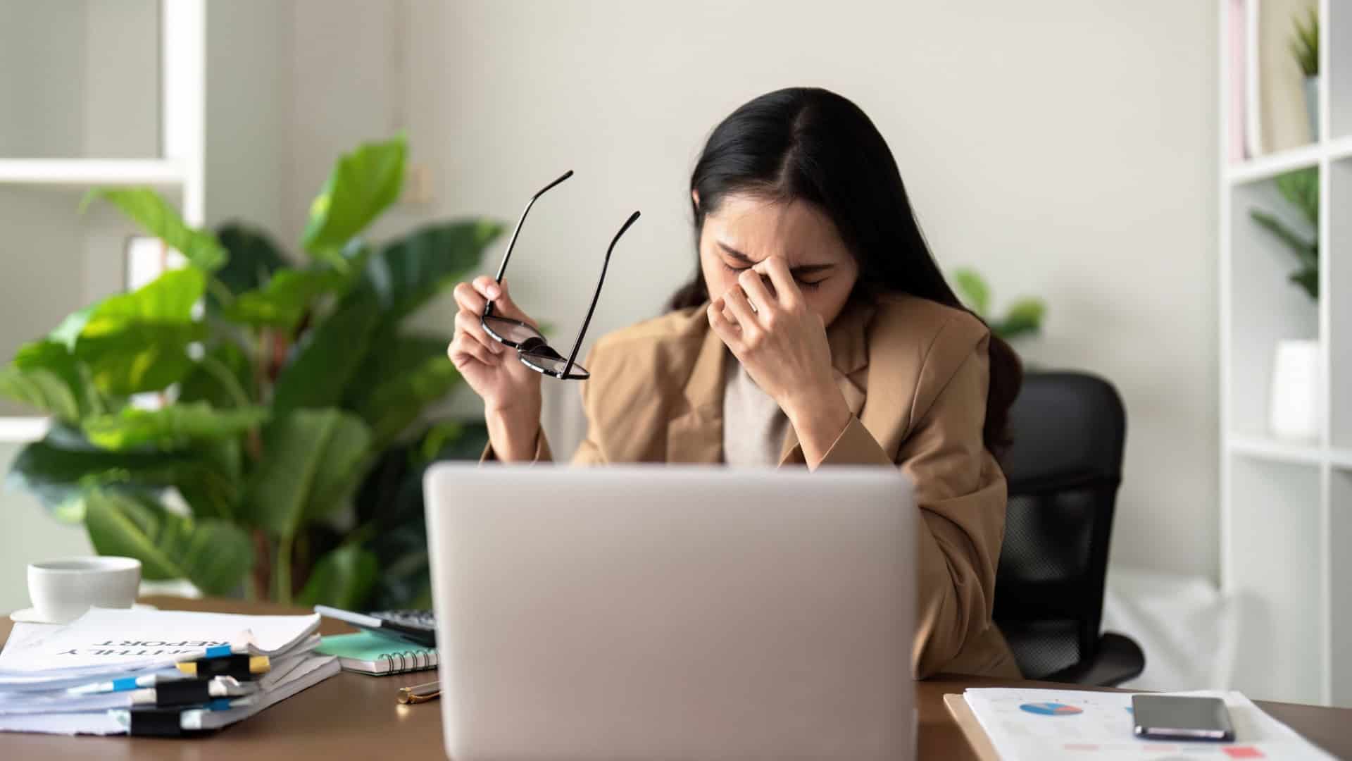 Mulher estressada sentada com a mão na cabeça na frente do notebook