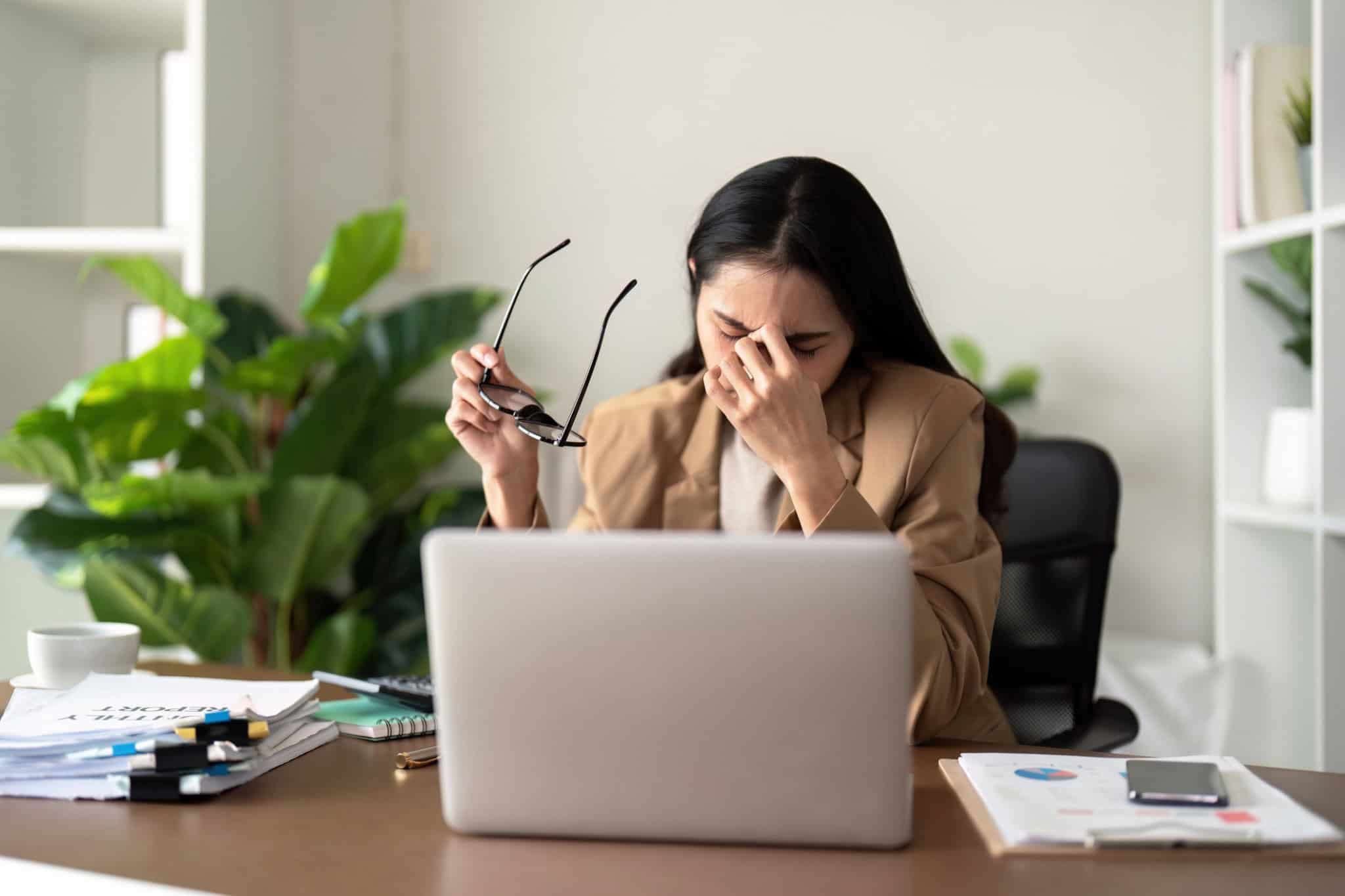 Mulher estressada sentada com a mão na cabeça na frente do notebook