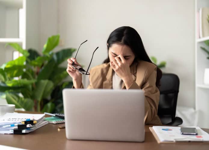 Mulher estressada sentada com a mão na cabeça na frente do notebook