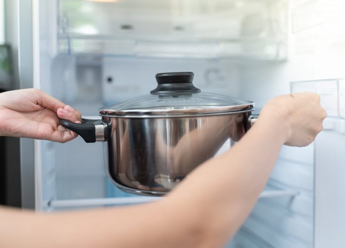 Mulher coloca panela de comida na geladeira