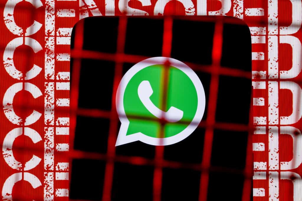 Logo do WhatsApp em um smartphone sendo mostrado atrás de uma cerca de arame