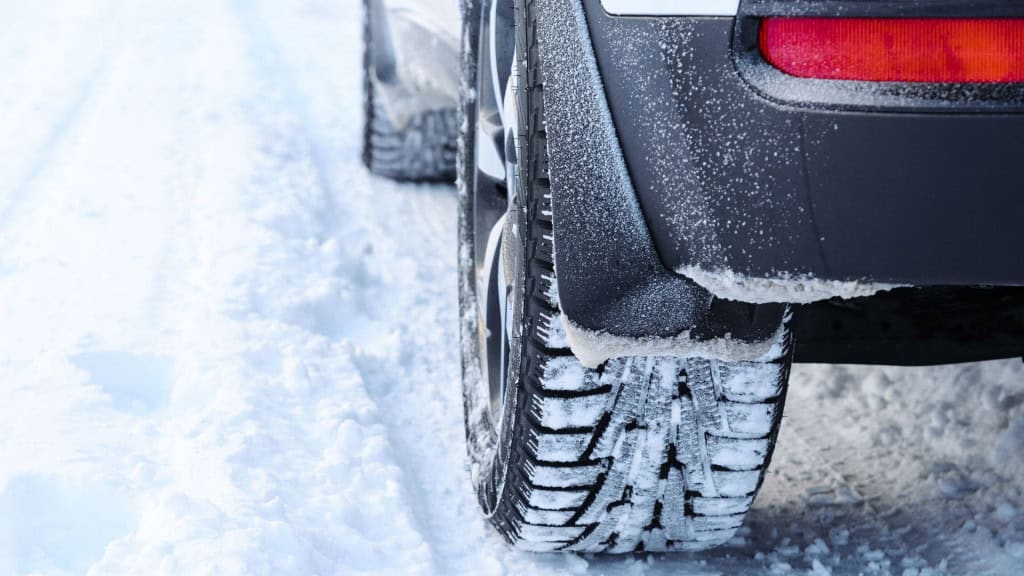 Pneus de carro em estrada com neve vistos em close.